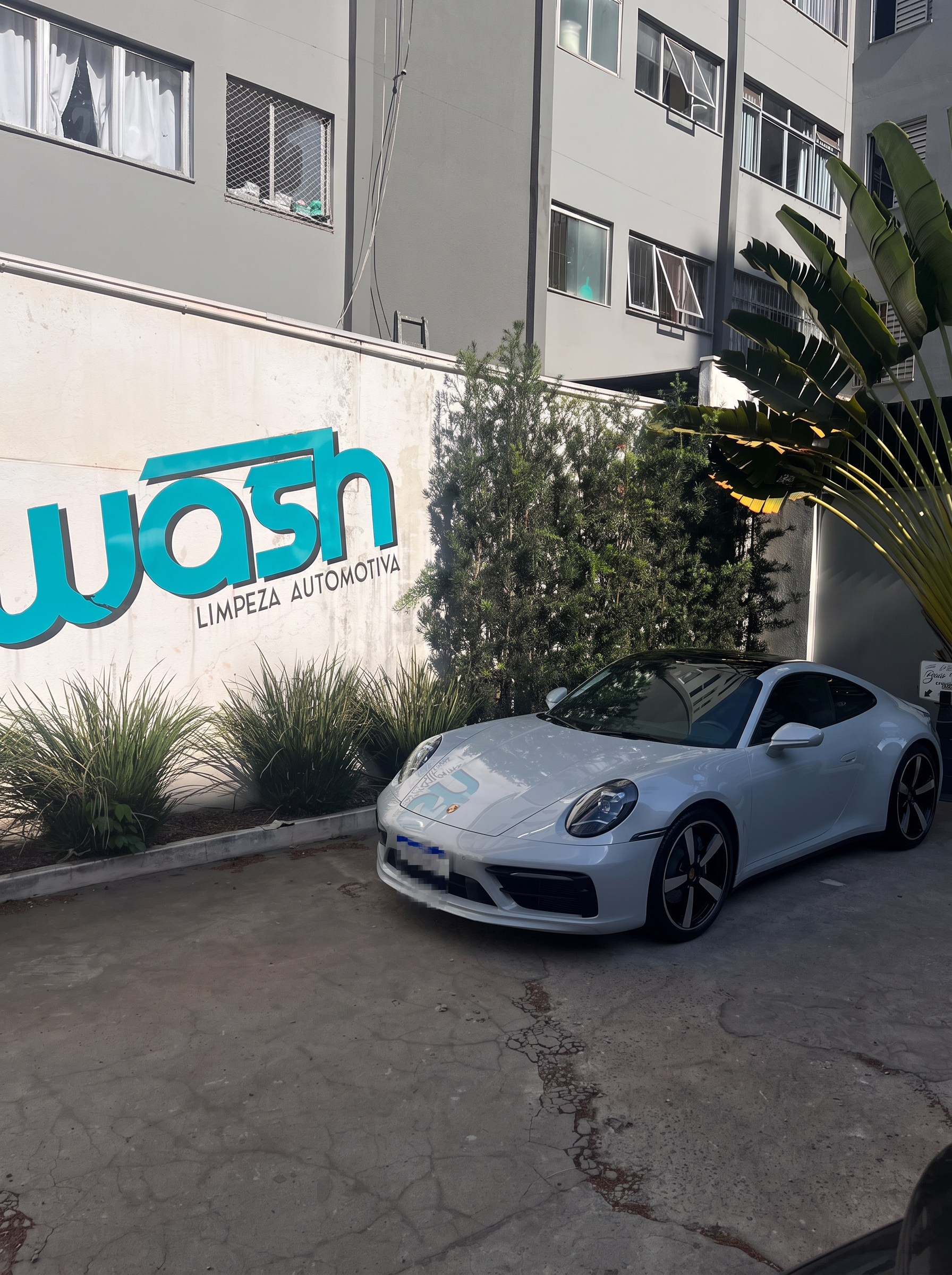 Porsche branco em frente ao muro com a logo da Wash